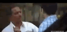 a man in a white shirt and tie is talking to another man in a blue shirt in a blurry photo .