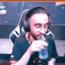 a man wearing headphones is drinking water from a bottle while sitting in a gaming chair .