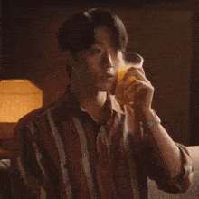 a man wearing a striped shirt is drinking a glass of orange juice