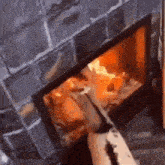 a person is standing in front of a fireplace with a brick wall and a fire coming out of it .