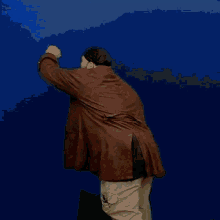 a man in a brown coat is standing in front of a blue background