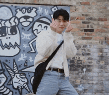 a man making a heart shape with his fingers in front of a graffiti wall