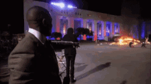 a man in a suit stands in front of a burning building at night