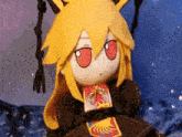 a stuffed animal with yellow hair and red eyes is sitting on a blanket .