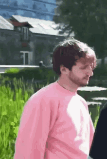 a man with a beard is wearing a pink sweater and standing in a field .