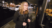 a woman wearing glasses and a black jacket is walking down a sidewalk