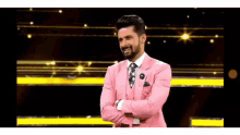 a man wearing a pink suit and tie is standing with his arms crossed .