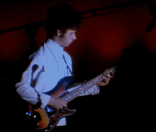 a man in a white shirt is playing a guitar in the dark