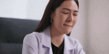 a close up of a woman in a lab coat making a funny face with her eyes closed .