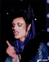 a drag queen is wearing a purple and black outfit with feathers