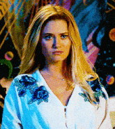 a blonde woman wearing a white shirt with blue flowers on the sleeves