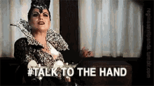 a woman is sitting at a table with a martini in her hand and the words `` talk to the hand '' written on the screen .