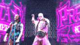 two wrestlers are standing next to each other on a stage in front of a pink wall .