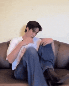 a man in a white shirt and blue jeans is sitting on a couch