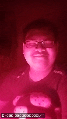 a man with glasses and a hello kitty shirt is standing in a dark room