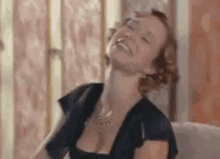 a woman in a black dress is sitting on a couch laughing with her eyes closed .