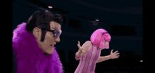 a man wearing a purple fur coat and sunglasses is standing next to a woman wearing pink hair .