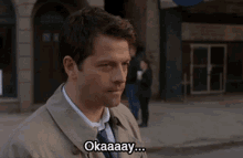 a man in a trench coat and tie says " okaaay "