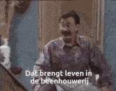 a man with glasses and a mustache is sitting at a table with the words dat brengt leven in de beenhoeverij
