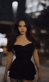 a woman in a black dress is standing on a street at night