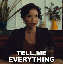 a woman sitting at a table with a glass of juice and a plate of food says tell me everything