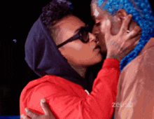 a man with blue hair is kissing a woman in a red shirt