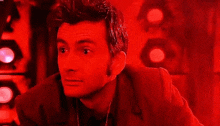 a man in a suit and tie is standing in a dark room with red lights behind him .