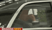 a man is sitting in a car with a breaking news headline above him