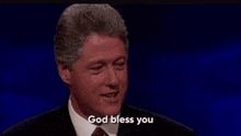 a man in a suit and tie is saying `` god bless you '' while standing in front of a blue background .