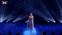 a woman singing on a stage with an x on the bottom left
