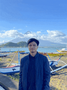 a man stands in front of a lake with boats in the background and a mountain in the background