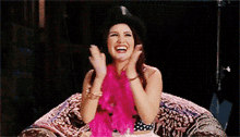 a woman wearing a hat and pink boa is sitting on a couch