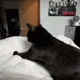 a black cat laying on a bed with a sopranos poster on the wall behind it