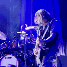 a man is playing a guitar in front of a tama drum set