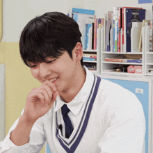 a young man wearing a white shirt and a blue vest is smiling in front of a bookshelf with chanel on it