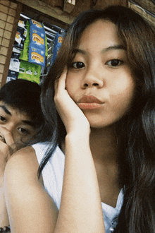 a girl holds her hand to her face while a boy looks on behind her