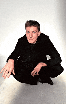 a man in a black jacket is squatting down with his hands outstretched