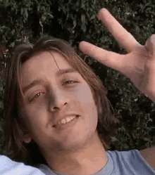 a young man with long hair is giving a peace sign with his fingers .