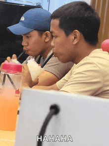 two men sit at a table with a bottle of orange juice and a sign that says ' hahaha ' on it
