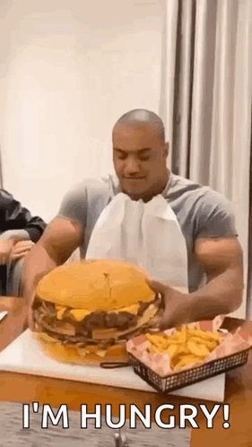 a muscular man is eating a giant hamburger and french fries .