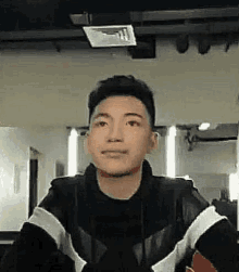 a young man in a black jacket is looking at the camera .