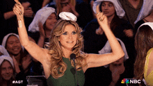 a woman in a green dress is giving a thumbs up in front of a crowd with nbc written on the bottom right