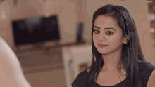 a woman in a black shirt is smiling in front of a tv screen that says voot in the corner