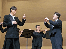 a man in a tuxedo is giving directions to a group of violinists