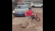 a person is riding a bike in front of a car with a red umbrella .