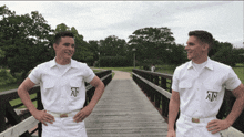 two men wearing white shirts with the letters ain on them stand on a wooden bridge