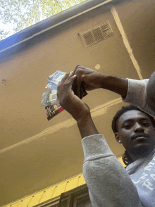 a man wearing a grey sweatshirt with the letter h on it holds up a stack of money