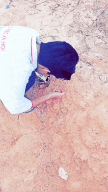 a boy wearing a white shirt with the word ho on the back is kneeling down in the dirt