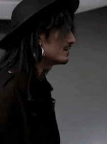 a man with long hair wearing a hat and earrings