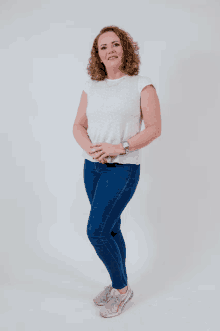a woman in a white shirt and blue jeans stands with her hands on her hips
